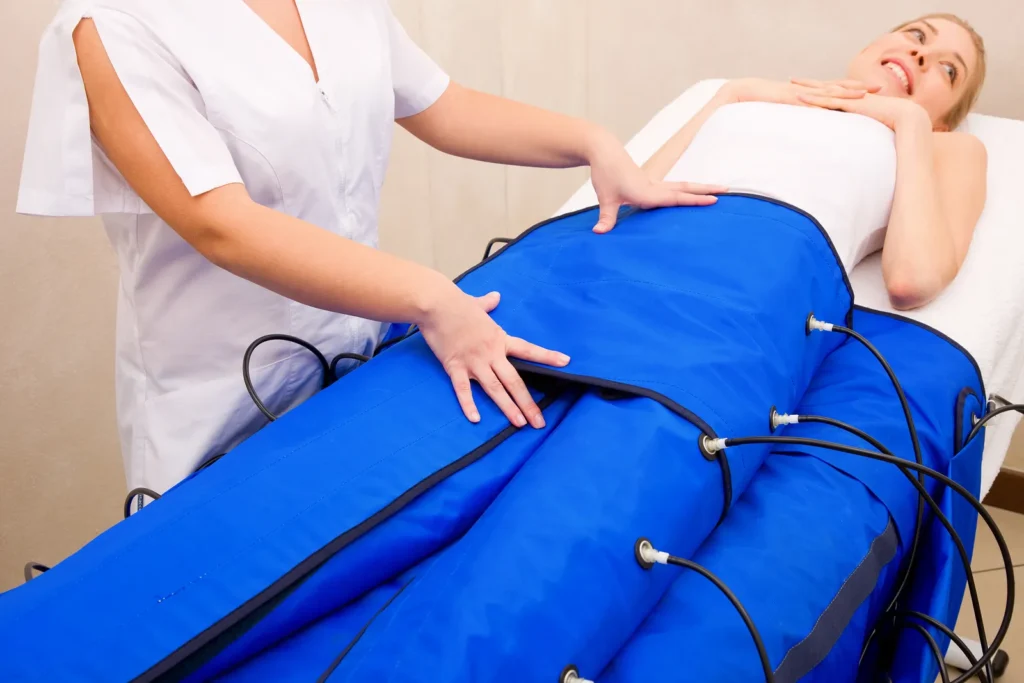 mujer recibiendo tratamiento de presoterapia con botas de compresión neumática azules en piernas para drenaje linfático