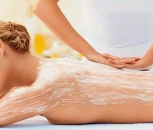 mujer recibiendo tratamiento de peeling corporal exfoliante en la espalda aplicado por esteticista profesional