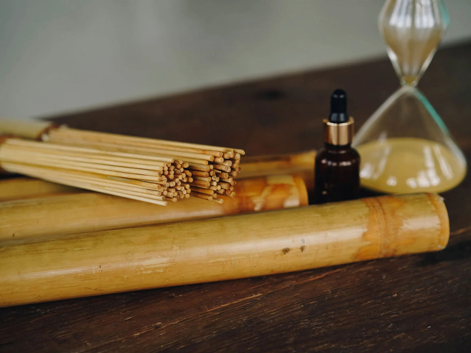 cañas de bambú sobre mesa de madera con aceite esencial y reloj de arena para sesión de bambuterapia