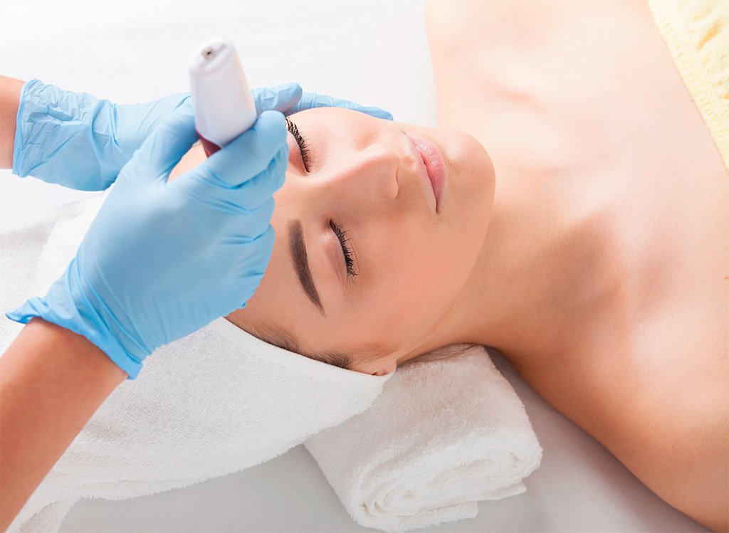 esteticista realizando tratamiento de mesoterapia inyectable en mano de paciente con guantes azules en centro estético profesional