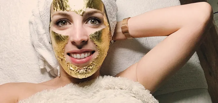 mujer relajada con mascarilla facial dorada de 24 kilates aplicada en rostro para tratamiento de lujo rejuvenecedor y revitalizante